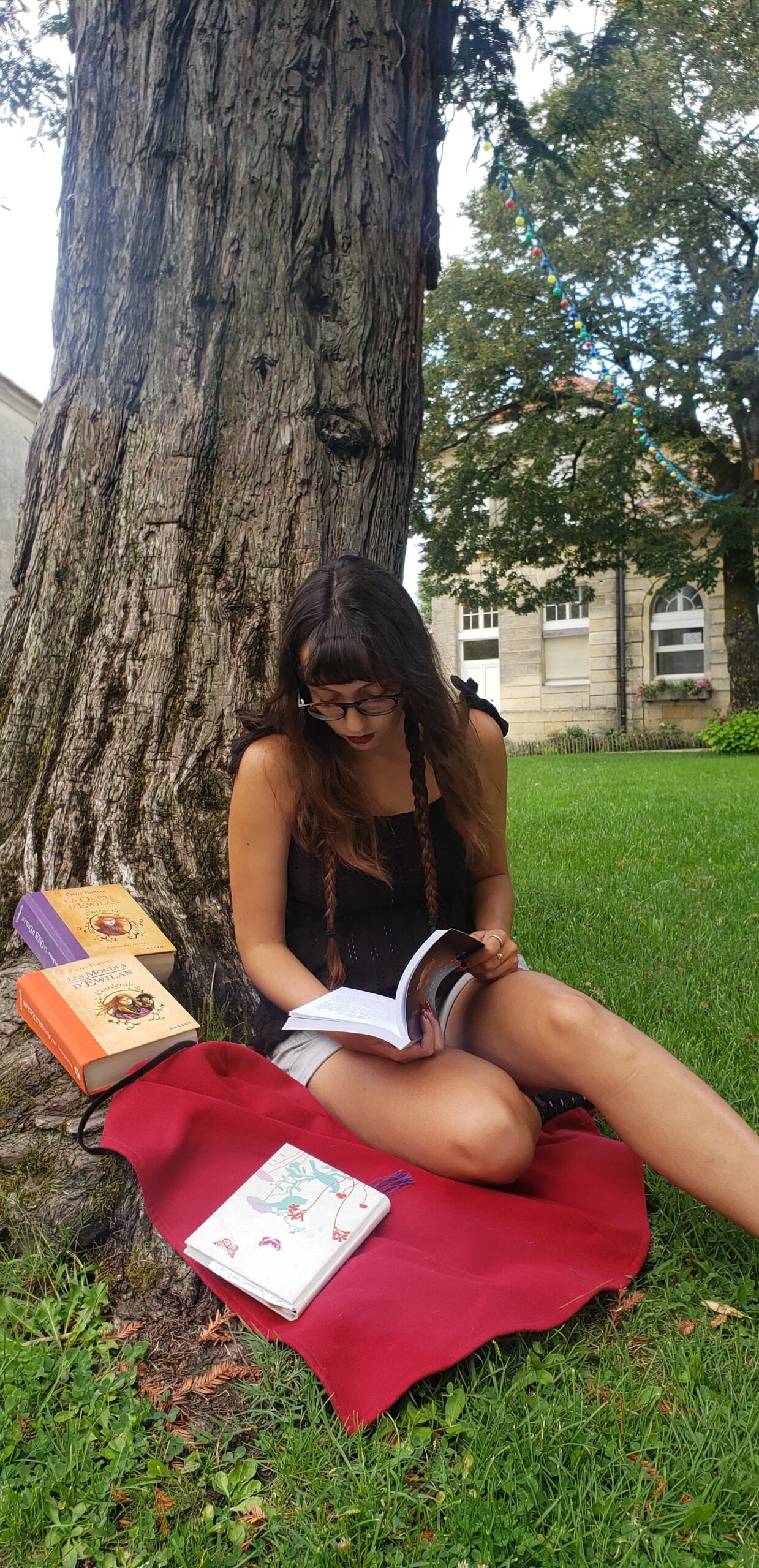 femme contre un arbre marron sur une cape rouge, sur l'herbe verte qui lient des livres